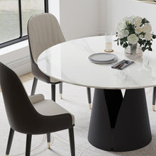 Charger l'image dans la galerie, Modern dining area featuring a round marble table with a unique black base, accompanied by two stylish chairs with beige and dark gray upholstery. The table is set with elegant tableware and a floral centerpiece, creating a sophisticated and inviting atmosphere