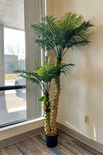 Load image into Gallery viewer, Artificial palm tree with multiple fronds displayed by a large window, adding tropical ambiance to the space.
