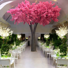 Load image into Gallery viewer, Exquisite artificial tree with vibrant pink blossoms, serving as a breathtaking centerpiece in a beautifully decorated wedding venue with lush greenery and floral arrangements. Are these rental trees available in different colors to match event themes?