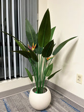 Charger l'image dans la galerie, Ivory round planter with a smooth matte finish, holding a vibrant artificial bird of paradise plant with broad green leaves and colorful flowers, placed indoors near a window. Does this planter come with a protective inner lining?