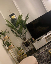 Charger l'image dans la galerie, Artificial palm tree placed in a modern living room next to a TV, adding a touch of greenery and style to the space.