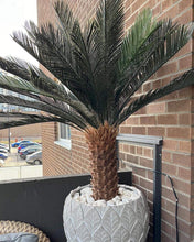 Charger l'image dans la galerie, Artificial palm tree in a decorative planter with white stones, adding a tropical touch to an outdoor balcony space.