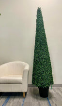 Charger l'image dans la galerie, A tall, cone-shaped artificial topiary tree in a black pot is positioned next to a white armchair in an indoor setting, creating a simple yet elegant display.