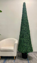 Charger l'image dans la galerie, A tall, cone-shaped artificial topiary tree in a black pot is positioned next to a white armchair in an indoor setting, creating a simple yet elegant display.