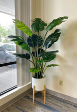 Load image into Gallery viewer, Large artificial monstera plant with vibrant green, split leaves, displayed in a sleek white pot on a wooden floor, enhancing the indoor decor with a tropical touch