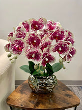 Charger l'image dans la galerie, A striking arrangement of white and magenta-spotted artificial orchids in a shiny silver planter, placed on a wooden side table. Frequently asked question: What are the best ways to clean and maintain artificial orchid arrangements?