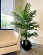 Charger l'image dans la galerie, Artificial palm tree with green fronds, placed in a sleek black pot next to a white sofa, adding a natural touch to a modern, well-lit living room.