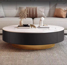 Charger l'image dans la galerie, Elegant round coffee table with a white marble top and a black base featuring a gold accent at the bottom. The table is styled with decorative items and placed in front of a beige sofa with patterned pillows, creating a luxurious and modern living room setting.