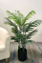 Charger l'image dans la galerie, Artificial palm tree in a black planter, placed next to a cream armchair, creating a fresh and modern indoor décor setting.