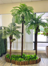 Charger l'image dans la galerie, "Artificial palm trees with coconuts set up indoors, surrounded by lush greenery and enclosed in a wooden planter, creating a vibrant tropical display perfect for brightening up any indoor space."