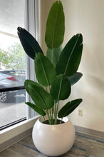 Load image into Gallery viewer, Large artificial bird of paradise plant with lush green leaves in a white round pot placed near a window in a modern indoor setting