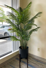 Charger l'image dans la galerie, Elegant artificial palm tree in a black pot on a gold stand, placed next to a window.
