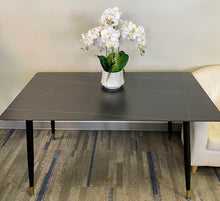 Charger l'image dans la galerie, What are the best simple yet elegant dining tables? This minimalist black dining table with gold-accented legs is styled with a white orchid centerpiece, creating a clean and sophisticated look. The table's sleek design makes it perfect for modern dining spaces or home offices.