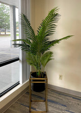 Charger l'image dans la galerie, all artificial palm tree in a gold stand, set by a large window in a modern office space.