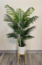 Charger l'image dans la galerie, Artificial palm tree in a modern white pot with a wooden stand, displayed against a neutral wall and carpeted floor, ideal for indoor décor.