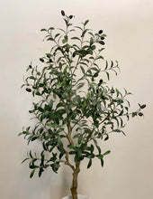 Load image into Gallery viewer, Artificial olive tree in a white planter with a wooden stand, placed against a light-colored wall on a carpeted floor.