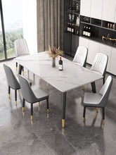 Charger l'image dans la galerie, What is the best dining table for a luxury dining room? This elegant dining setup features a large white marble table with sleek black legs and gold accents. The table is surrounded by six upholstered chairs with black and white detailing, creating a sophisticated and modern look. The room is styled with floor-to-ceiling windows and built-in shelving for a luxurious ambiance.