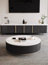 Charger l'image dans la galerie, Modern living room with a round coffee table featuring a white marble top and black base. The table is placed on a geometric-patterned rug and in front of a sleek black TV stand with gold accents. Decorative items, including a lamp and sculptures, are arranged on the TV stand, creating a minimalist and sophisticated space