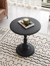 Charger l'image dans la galerie, A round, black pedestal coffee table with a sturdy, decorative base sits on a patterned black-and-white rug. A green coffee cup and saucer rest on a book atop the table, creating a cozy, stylish setting near a window with soft, sheer curtains that allow natural light into the room.