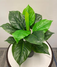 Charger l'image dans la galerie, The image shows a potted artificial plant with broad, vibrant green leaves arranged in a compact form. The leaves range in shades from light to dark green, giving the plant a lifelike appearance. It sits atop a round, white tabletop, adding a refreshing pop of greenery to the minimalist space. The plant's natural look makes it an ideal decorative piece for desks or tables in both home and office settings.