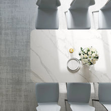 Charger l'image dans la galerie, Modern white marble dining table surrounded by gray upholstered chairs in a contemporary dining room setting. The table features a vase with white flowers and a small bowl, showcasing a minimalist yet elegant design