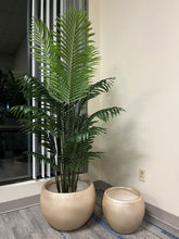Charger l'image dans la galerie, Set of two gold metallic round planters with a smooth finish, one holding a tall artificial palm plant with lush green leaves, placed indoors near a window. Are these planters rust-resistant and suitable for outdoor use?