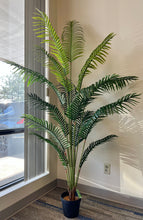 Charger l'image dans la galerie, Artificial palm tree in a black pot by a window, with lush green fronds creating natural shadows, perfect for home or office decor.