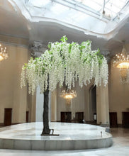 Charger l'image dans la galerie, A tall, elegant artificial Wisteria tree in white, featuring dense foliage and hanging blooms, placed inside a storage area with boxes in the background.