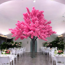 Load image into Gallery viewer, A vibrant artificial pink blossom tree standing in a spacious, elegant hall with white chairs and floral decorations, ideal for weddings or luxury events. Can this pink blossom tree be customized in size to fit smaller venues?