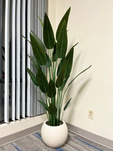 Charger l'image dans la galerie, Close-up of an ivory round planter with a smooth matte finish, holding an artificial palm plant with vibrant green leaves, placed indoors near a window. Does this planter have a built-in drainage system?