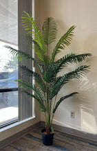 Charger l'image dans la galerie, Artificial palm tree in a black pot by a window, with lush green fronds creating natural shadows, perfect for home or office decor.