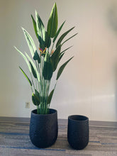 Charger l'image dans la galerie, Set of two black planters with a crater-like textured design, one holding a tall artificial bird of paradise plant with vibrant green leaves and orange flowers, placed indoors on a carpeted floor. Are these planters available in multiple finishes?