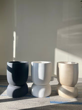 Charger l'image dans la galerie, Set of three cylindrical planters in black, white, and gold finishes, displayed empty indoors on a carpeted floor in natural light. Are these planters available in additional colors or finishes?
