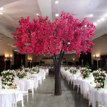 Load image into Gallery viewer, Stunning artificial tree with vibrant red blossoms, elegantly placed as a centerpiece in a lavishly decorated wedding venue featuring white chairs, floral arrangements, and ambient lighting. How do these rental trees enhance the beauty of large-scale weddings?