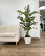Charger l'image dans la galerie, Artificial palm plant in a modern white textured planter placed beside a minimalist beige armchair on a wooden floor. Common questions: What are the benefits of artificial plants for office spaces? How to style artificial plants in living rooms? What type of planter complements minimalist decor?