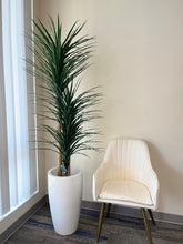 Charger l'image dans la galerie, Artificial Yucca Plant-5.8ft. Modern office corner with a tall indoor plant in a white planter, paired with a chic white chair with gold legs, against a light beige wall.