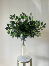 Load image into Gallery viewer, Realistic artificial greenery arranged in a tall clear glass vase filled with water, placed on a sleek marble pedestal. Perfect for adding a natural touch to weddings and events. Can this greenery elevate your venue’s aesthetics?