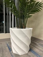Charger l'image dans la galerie, modern white spiral-patterned planter containing a lush green plant with long, elegant fronds, placed on a carpeted floor near a window with vertical blinds.