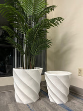 Charger l'image dans la galerie, A large, lush green plant displayed in a white, spiral-patterned planter, accompanied by a smaller, matching empty planter, set indoors on a carpeted floor near vertical blinds.