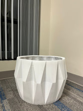 Charger l'image dans la galerie, White planter with a faceted geometric design, displayed empty indoors near a window on a carpeted floor. Does this planter include a drainage hole for excess water?