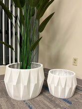 Charger l'image dans la galerie, Set of two white faceted geometric planters, one holding a tall artificial plant with lush green leaves, placed indoors near a window on a carpeted floor. Are these planters made of durable materials for long-term use?