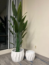 Charger l'image dans la galerie, Set of two white faceted geometric planters, one holding a tall artificial plant with lush green leaves, placed indoors near a window on a carpeted floor. Are these planters made of durable materials for long-term use?