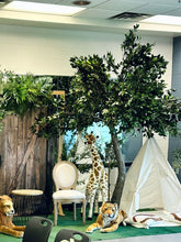 Charger l'image dans la galerie, A 10ft artificial Ficus tree with dense, vibrant green leaves, ideal for creating a jungle-themed atmosphere, surrounded by floral decorations and boxes in an indoor setting.