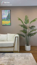 Charger et lire la vidéo dans la visionneuse de la Galerie, Elegant living room setting featuring a lush green palm plant in a black pot beside a modern white sofa with gold accents.