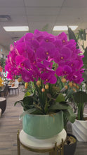 Load and play video in Gallery viewer, A vibrant artificial orchid arrangement in a bright fuchsia color, displayed in a modern white planter. Frequently asked question: How do I maintain artificial orchids to keep them looking fresh and dust-free?