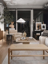Charger l'image dans la galerie, A stylish, modern living room with floor-to-ceiling windows at night, featuring a tall artificial olive tree, cozy textured armchair, and a mix of contemporary and classic decor, including a bust statue, wooden bench, and a soft neutral color palette