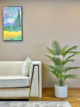 Charger l'image dans la galerie, Elegant living room setting featuring a lush green palm plant in a black pot beside a modern white sofa with gold accents.