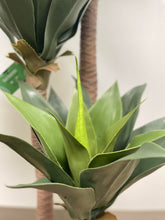 Charger l'image dans la galerie, Close-up shot of the base of an artificial yucca plant, featuring realistic green leaves and a textured faux trunk, showcasing the intricate detail for indoor home or office decor