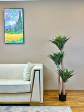Charger l'image dans la galerie, a cream-colored sofa with a faux yucca agave plant in a black pot next to it. The artificial plant adds greenery to the minimalist decor, enhancing the stylish interior design.