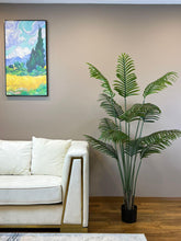 Charger l'image dans la galerie, Elegant living room setting featuring a lush green palm plant in a black pot beside a modern white sofa with gold accents.